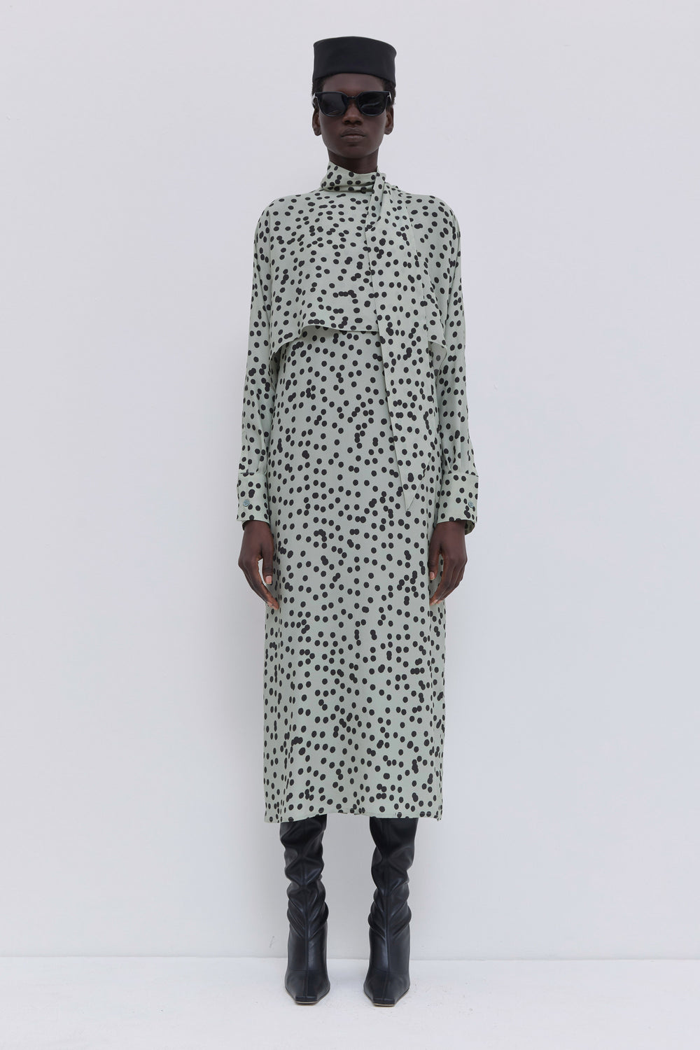 Model wearing a sage polka dot batwing sleeve dress with scarf collar, layered front panel and fluid midi silhouette by Christian Wijnants.