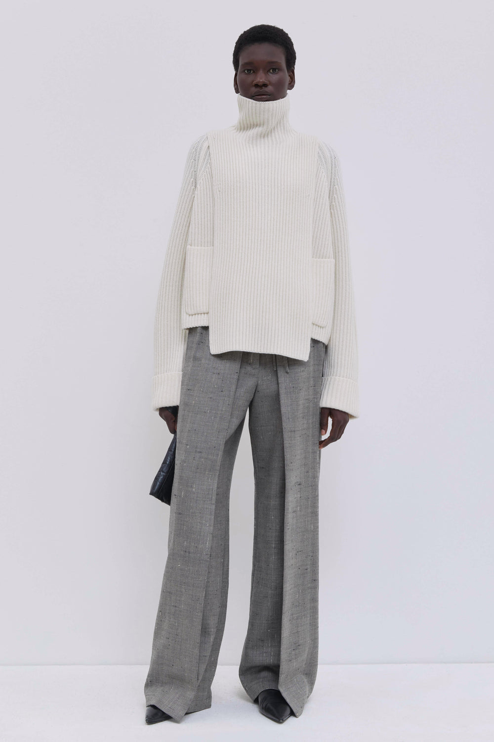 Cream ribbed merino wool and cashmere knit bib with oversized turtleneck, layered over wide-leg tailored trousers.